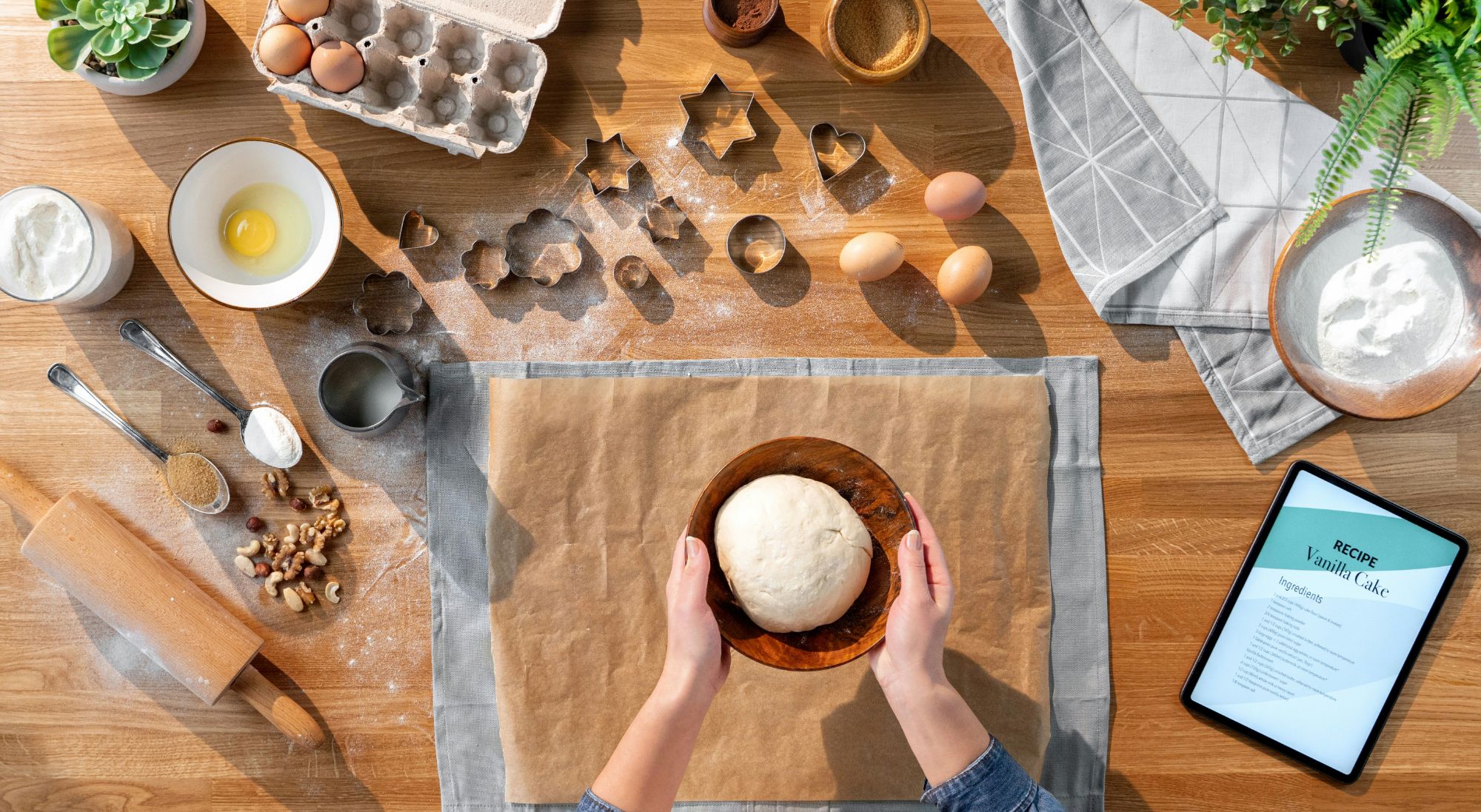Hands shaping bread dough on a wooden table surrounded by baking ingredients